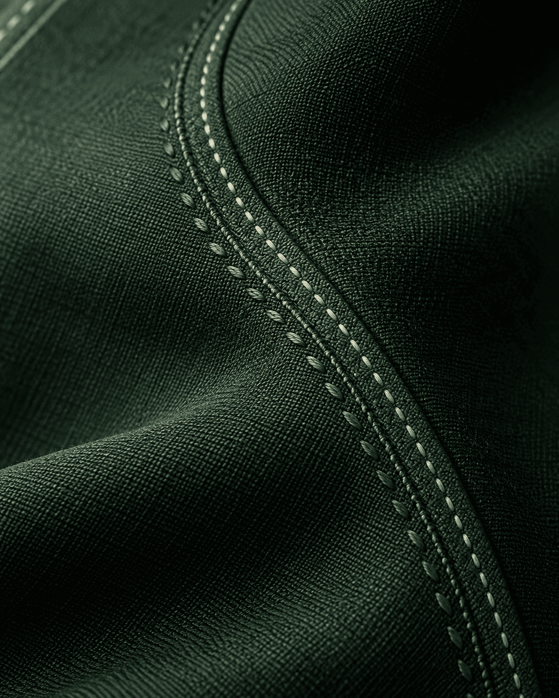 Macro d’un tissu vert profond, brodé de points précis et de fines surpiqûres ivoire.